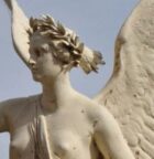 An elegant baroque-style angel statue holding a laurel wreath, captured outdoors with a clear sky backdrop.